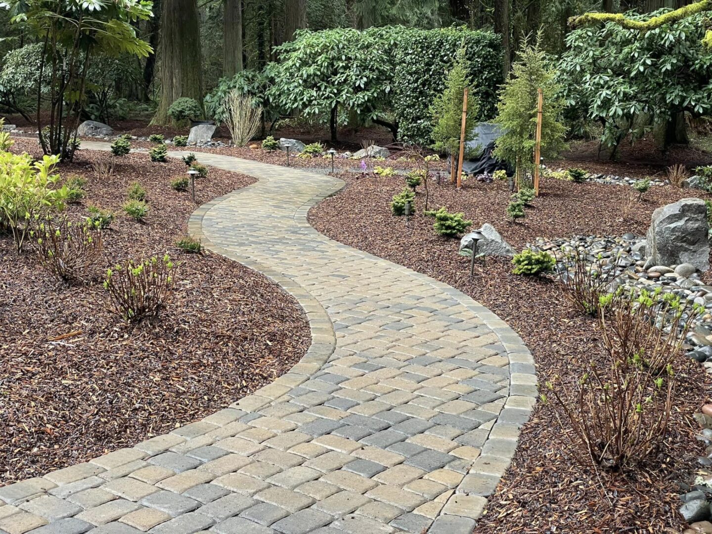 A garden path with brick and stone is surrounded by mulch.