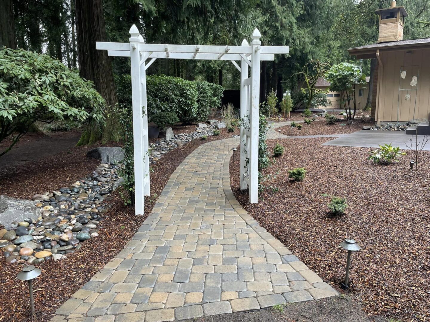 A walkway with brick and stone path leading to a wooden arbor.