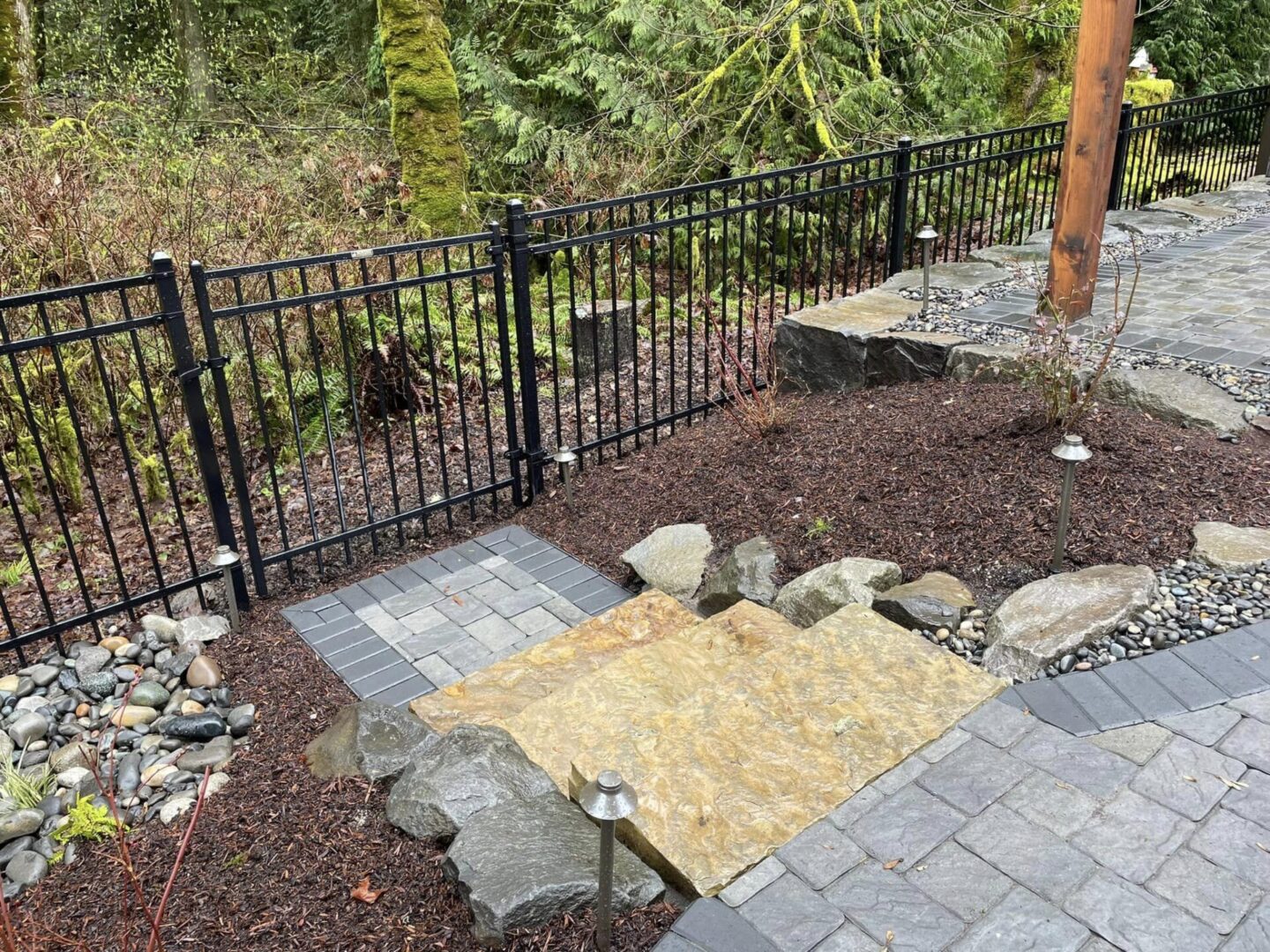 A walkway with rocks and grass next to a fence.