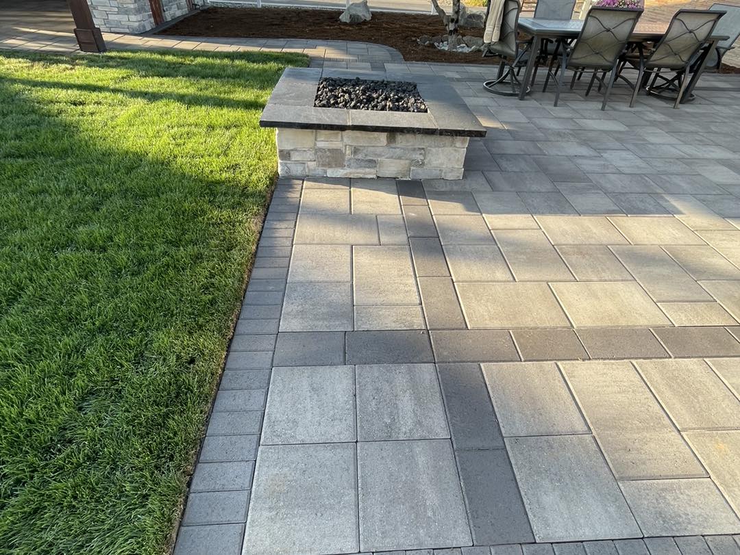 A patio with fire pit and grass in the middle of it.