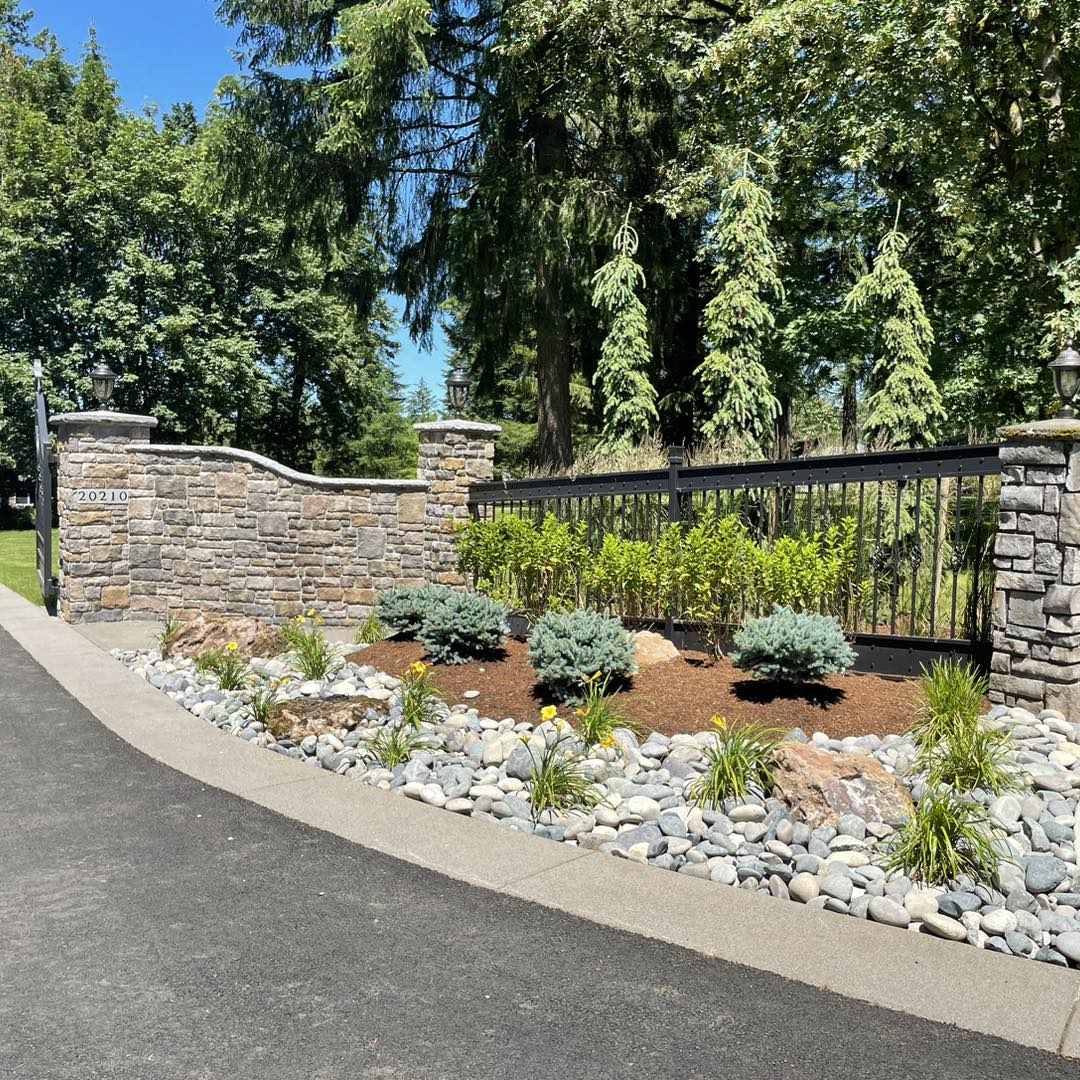 A driveway with stone walls and plants in the front.